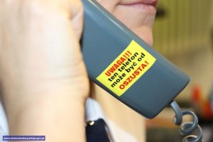 Kobieta trzyma słuchawkę przy uchu, na której jest napis: ten telefon może być od oszusta.